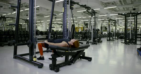 Athletic Girl in the Gym Doing Lying Exercises on Her Legs with a Barbell, Raises and Lowers the alt