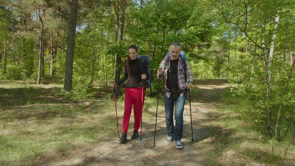 Cheerful Couple Backpackers with Hiking Poles Trekking in Forest alt