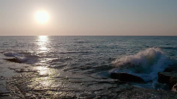 The waves crash against the rocky sea coast. Sunset.