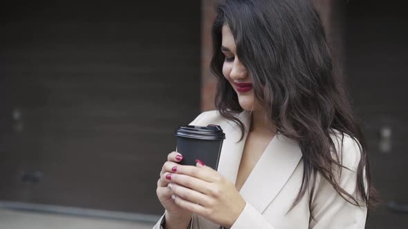 Beautiful Brunette with Blowing Hair and Claret Lips Admires a Cup of Drink alt