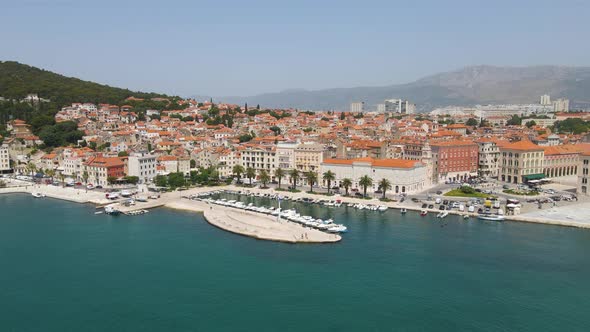 Aerial drone forwarding shot showing ancient roman town beside blue sea and mountains iin the backgr alt