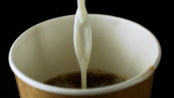 Spilling milk into a coffee drink. Black background. Close-up. alt