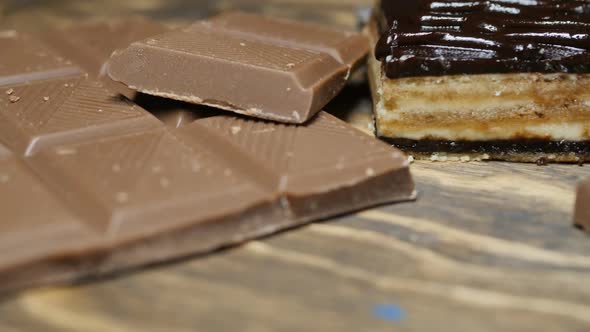 Dolly Shot of a Bar of Chocolate and a Slice of Chocolate Cake on a Wooden Background