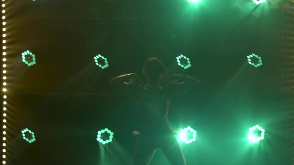 Silhouette of Dancing Young Women on Stage in a Dark Studio with Smoke and Neon Lighting. Green Neon alt