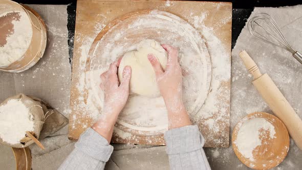 two female hands knead white wheat flour dough on a wooden board alt