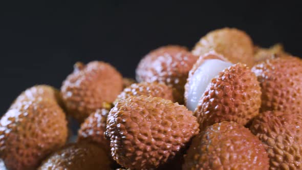 The Girl's Hand Takes Ripe Juicy Lychee Fruits on a Black Background alt