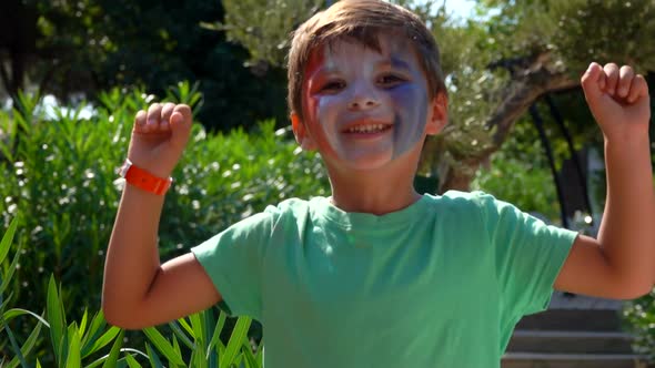 Boy is Jumping Cheerfully with Makeup Painted in the Colors of a French Flag alt