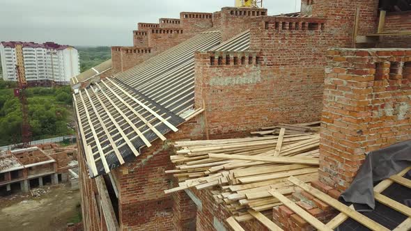 Aerial view of unfinished brick apartment building with wooden roof structure under construction. alt
