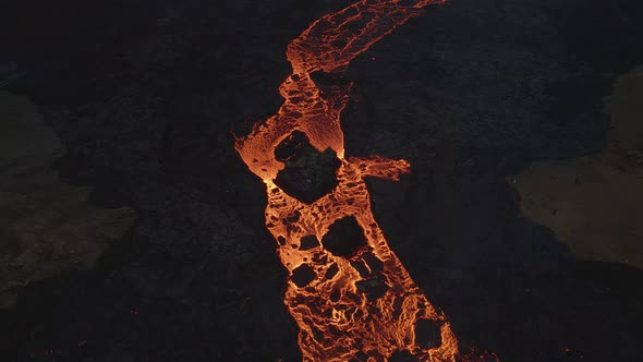 Aerial top-down forward over lava river flowing along black volcanic landscape alt