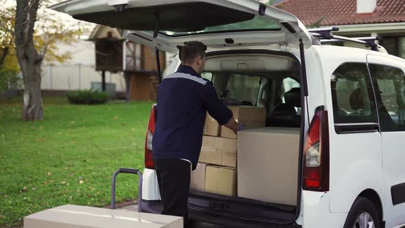 Handsome Man Takes Boxes Out of Trunk and Places Them in a Handcart alt