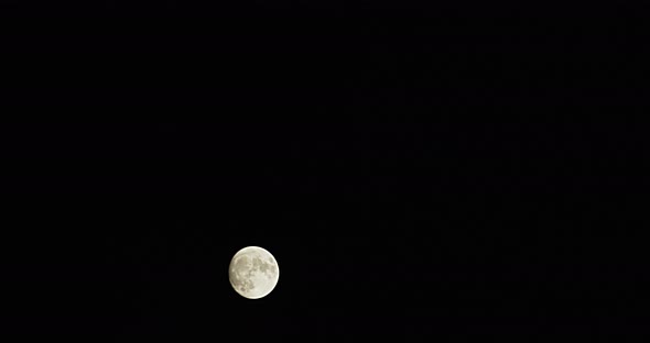 Time-lapse wide shot of a full moon as it rapidly rises from the lower left to the upper right. alt