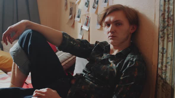 Young Man Sitting on Bed and Looking at Camera alt