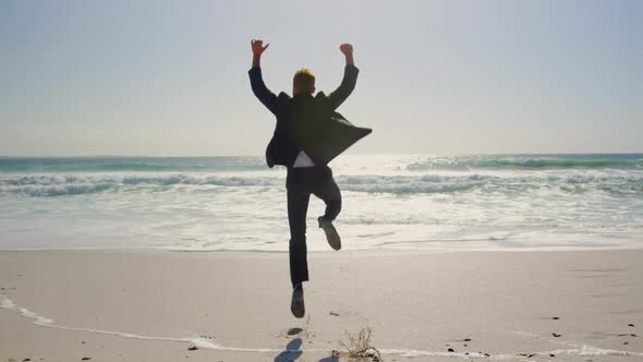 Businessman jumping on beach in the sunshine 