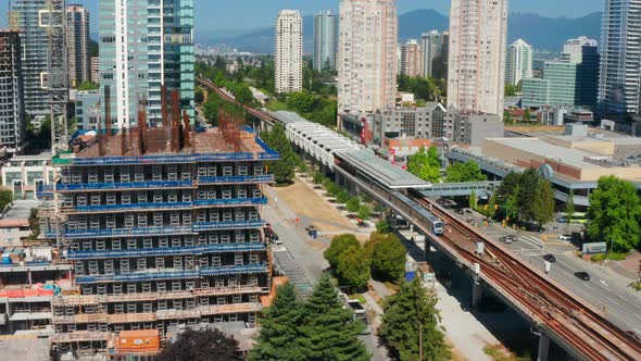 SkyTrain Transit Leaving At Metrotown Station With City Traffic In Burnaby, BC, Canada. - aerial pul alt