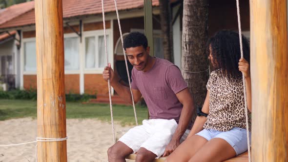 Romantic Young African Couple Swinging on a Beach Swing Smiling and Talking alt