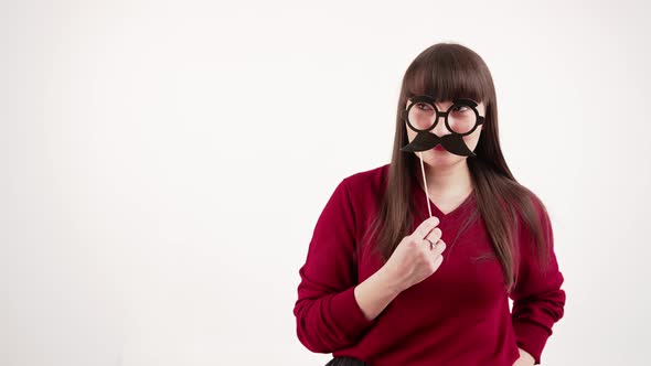 Young Caucasian Brunette Shushing While Holding Fake Mustache and Glasses Set in Front of Her Face alt