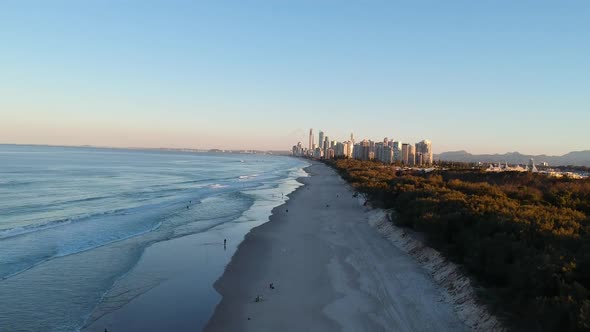 Sun setting on a beach with a golden city skyline glistening in the distance alt