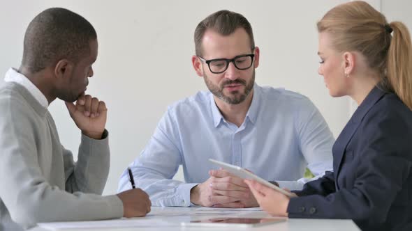 Mixed Race Businessperson Having Discussion While Using Tablet and Taking Notes alt