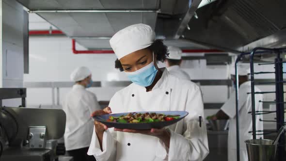 Portrait of african american female chef wearing face mask presenting dish alt
