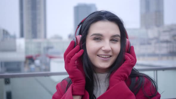 Close-up Face of Smiling Young Caucasian Girl with Black Hair and Green Eyes Putting on Earphones in alt