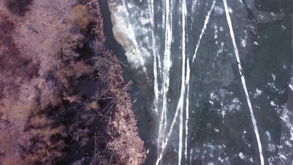 Aerial top down view of a lake with thin melted ice on the surface.