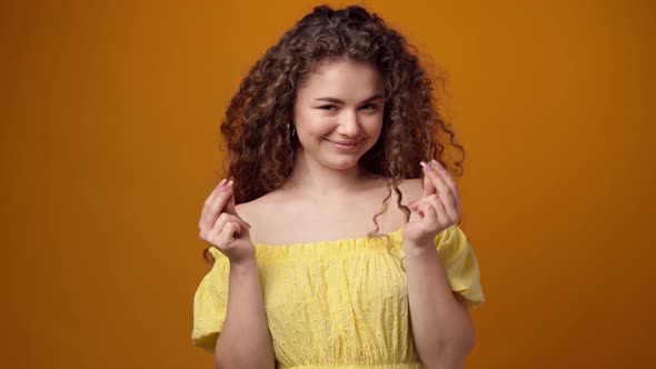 Young Woman Rubbing Fingers in Money Gesture Against Yellow Background