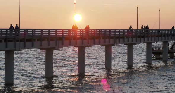 Silhouettes of People Walking on the Pier Against the Sunset. Local People Are Fishing, Tourists Are alt