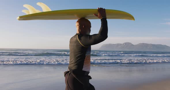Senior african american man walking with a surfboard on his head at the beach alt