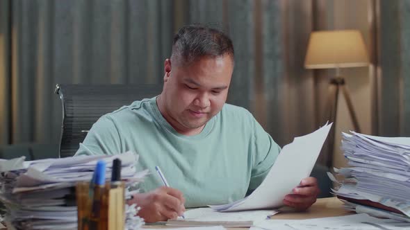 Close Up Of Smiling Fat Asian Man Enjoys Working With Documents At The Office alt