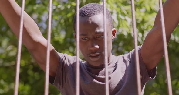 Close Up Portrait of Young Desperate African American Guy Standing Behind Metal Bars Outdoors alt