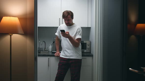Tired Guy Chat on Smartphone Standing in Kitchen Late in Evening alt
