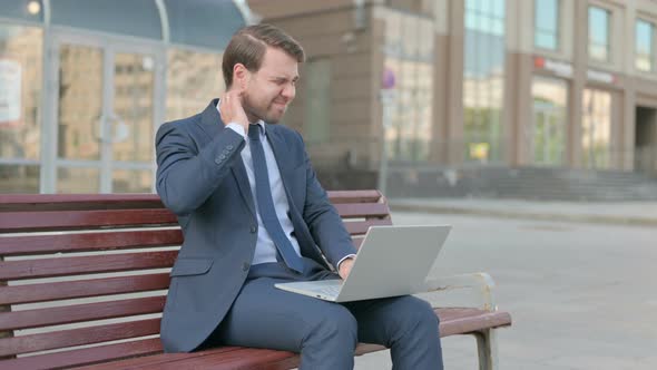 Businessman with Neck Pain Using Laptop while Sitting Outdoor on Bench alt