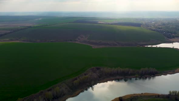 Flying above green, cultivated spring fields, lake