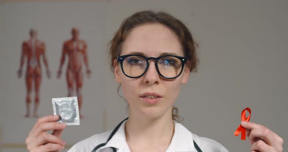 Female Doctor Holding Condom and Red Ribbon Warning Against Aids alt