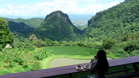 A woman drinking coffee and eating cake on balcony while enjoy watching a beautiful mountains view