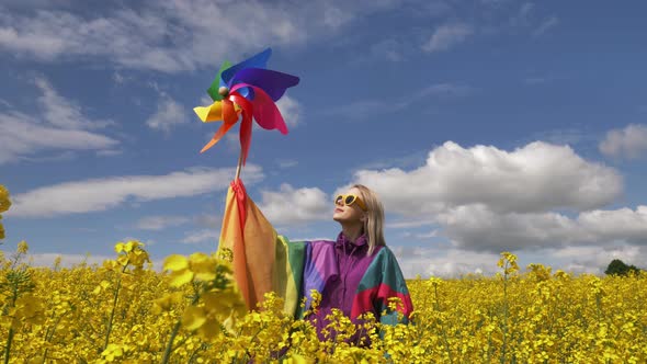 Female with LGBT rainbow flag and pinwheel on yellow rapeseed field in spring