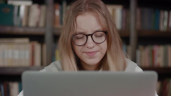 Close Up Tired Schoolgirl with Glasses Yawns Looking of Laptop Over Library Background alt
