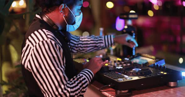 Black Dj playing music at cocktail bar outdoor while wearing face safety mask alt