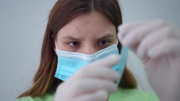 Headshot Front View of Focused Young Lab Assistant in Face Mask and Uniform Examining Test Tube alt