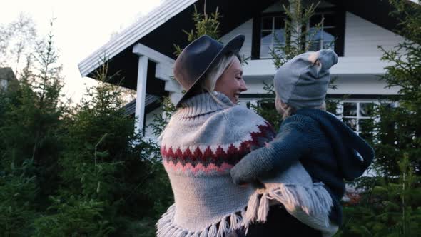 Close-up Shot of a Young Mother Holding and Playing with Her Baby Near the House at Sunset alt
