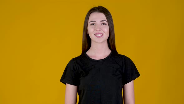 Positive young girl smiling and looking at the camera isolated on yellow background