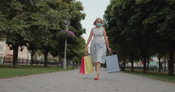 A Woman in a Protective Mask Walks Down the Street Carries Shopping Bags alt