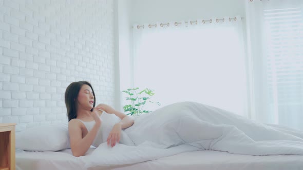 Woman stretching her arm after wake up on bed and looking outside windows alt