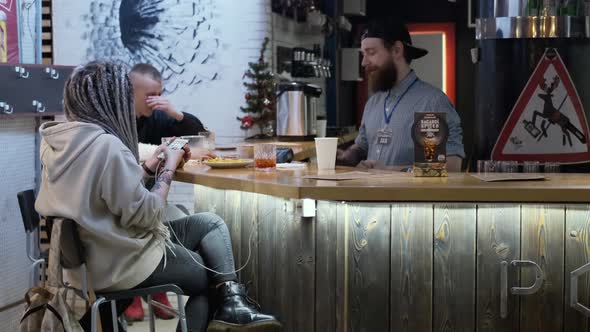 In the Bar Waiter Holds Credit Card Payment Machine and Hipster Girl Pays for Her Order Using a alt