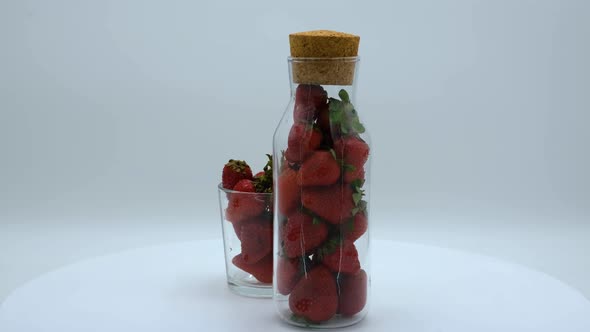Strawberries in a clear bottle and glass rotating on a white background. Strawberry ripe season
