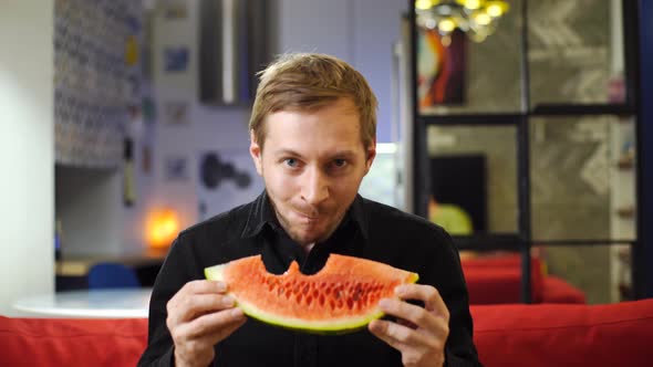 Portrait of young man eating a slice of juicy watermelon at home