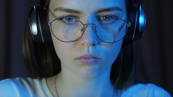 Closeup Portrait of Teenage Girl with Glasses and Wireless Headphones Looks at the Monitor alt