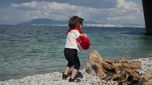 Stylish Child a Boy in a Black Jumpsuit and a Red Scarf Stands on the Beach alt