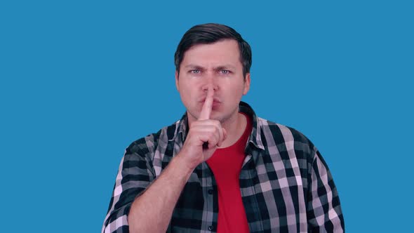 Man makes Shhh quiet, silence, secret gesture, isolated on a blue wall background.