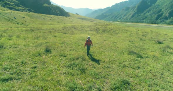Flight Over Backpack Hiking Tourist Walking Across Green Mountain Field. Huge Rural Valley at Summer alt